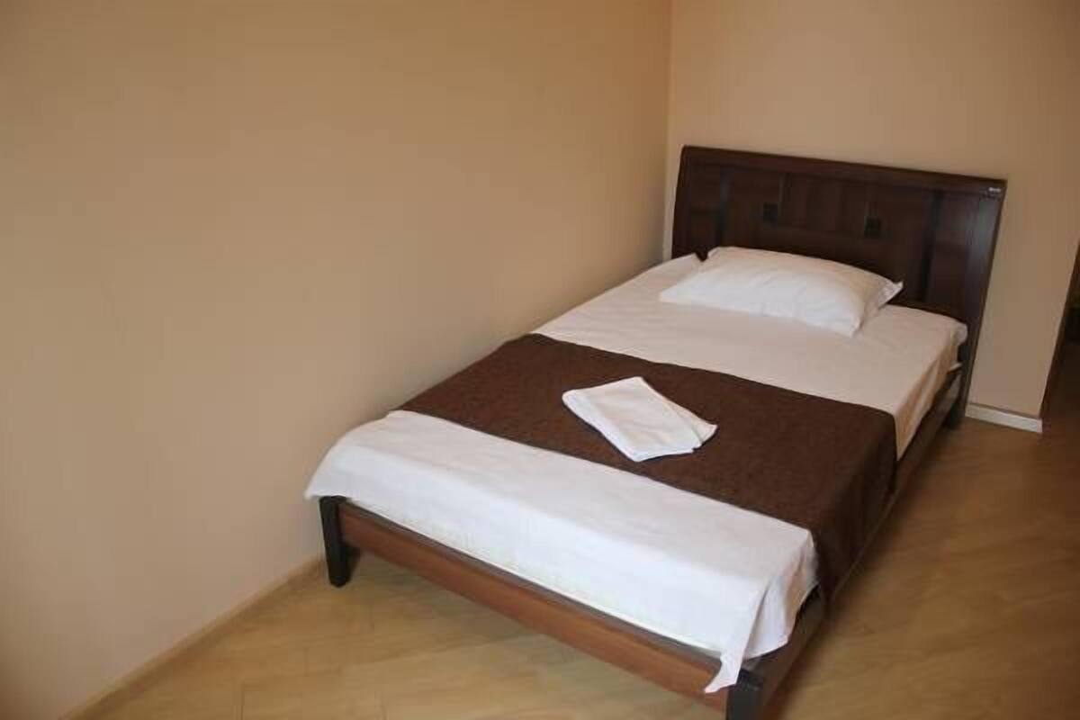 A single bed with a wooden headboard, a white bedspread, and a brown blanket.