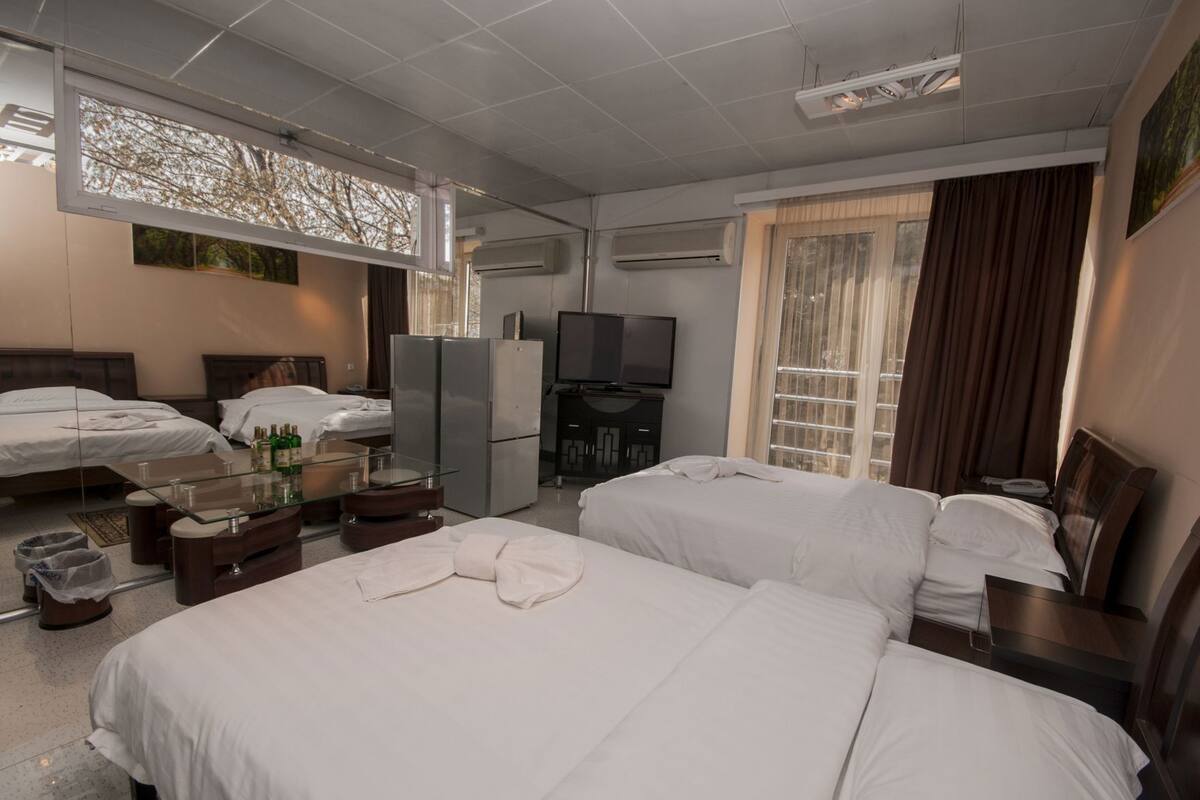 A hotel room with two beds, a TV, a minibar, and a window with curtains.
