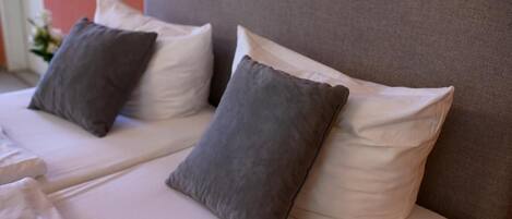 A bed with white linens and two pillows, one grey and one white.