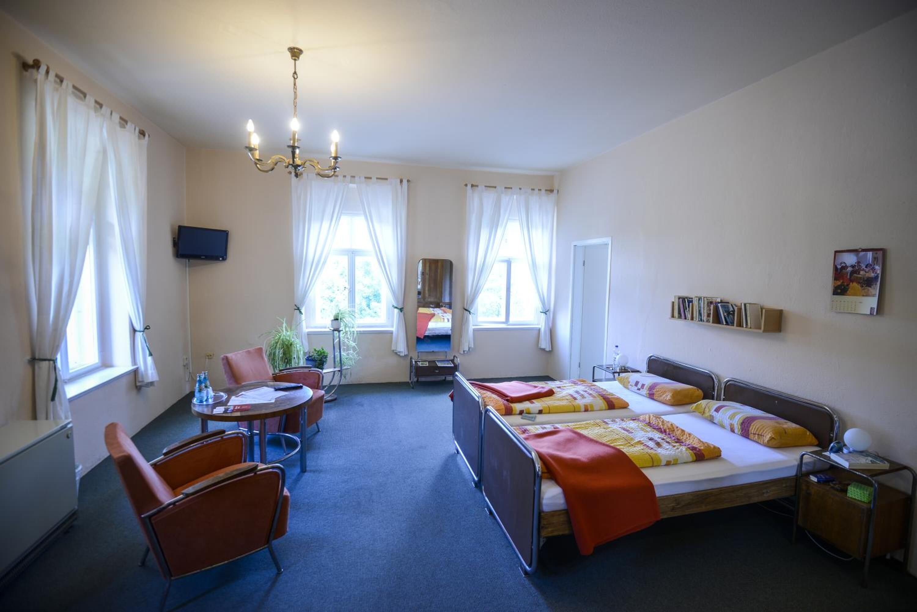 A hotel room with a bed, two chairs, a desk, a TV, and a window with curtains.