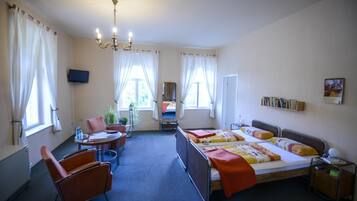 A hotel room with a bed, two chairs, a desk, a TV, and a window with curtains.