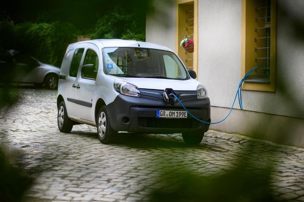Un coche blanco estacionado en una calle adoquinada con un cable de carga conectado.