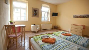A room with two beds, a chair, a table, and a TV.