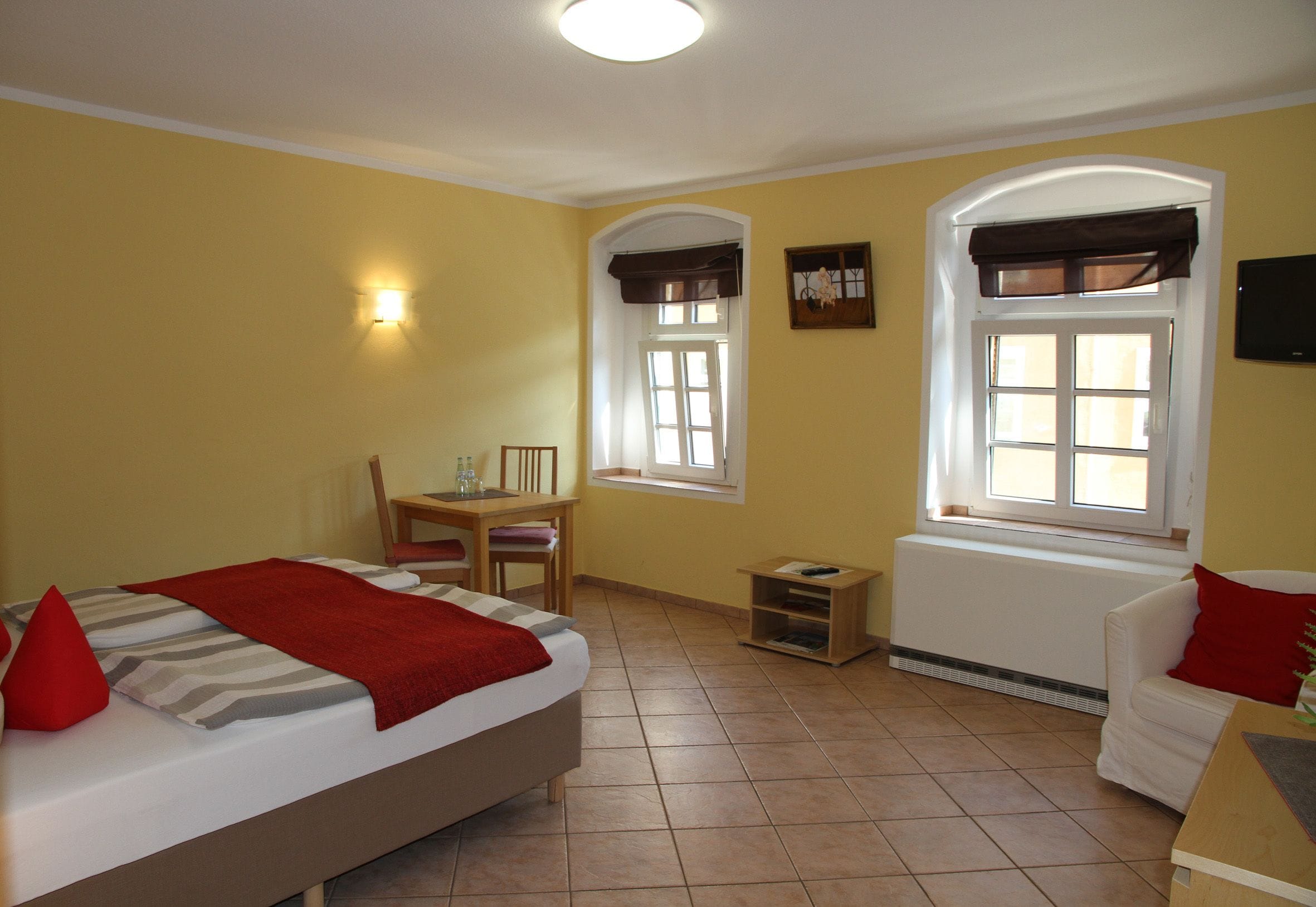 A bedroom with a bed, a desk, a chair, and two windows.