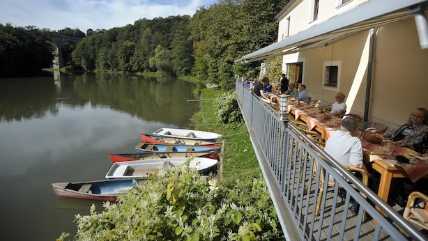 A lakeside restaurant with outdoor seating overlooking a calm lake, surrounded by lush greenery. - Obermühle Görlitz (Görlitz)