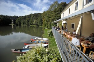 Ein Restaurant am Seeufer mit Außenbestuhlung und Blick auf den ruhigen See, umgeben von üppiger Vegetation.