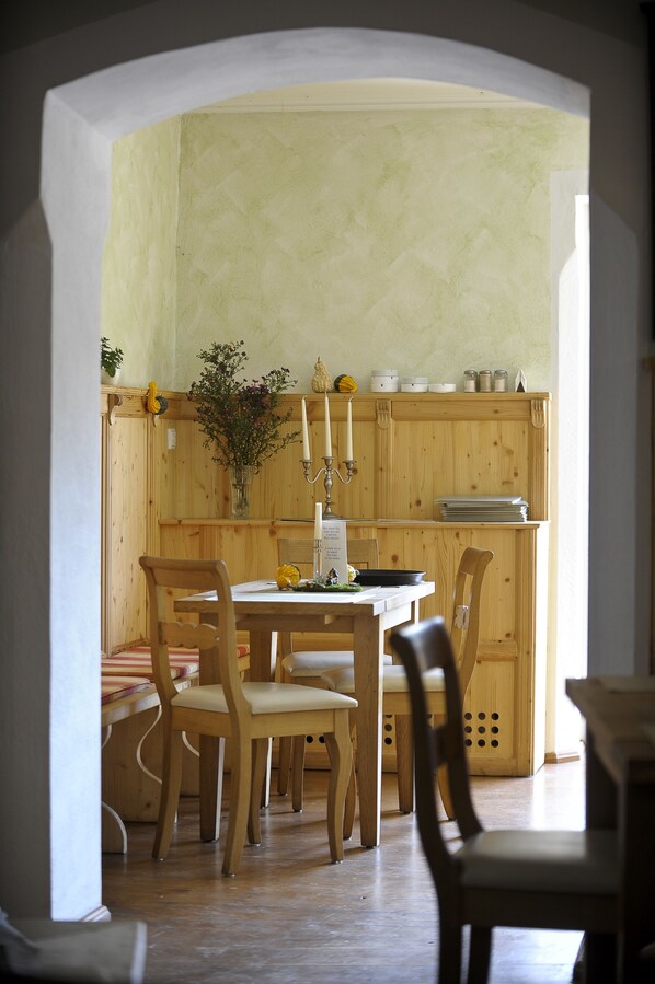 A wooden dining area with a table and chairs, a vase with flowers, and a candle on the wall.