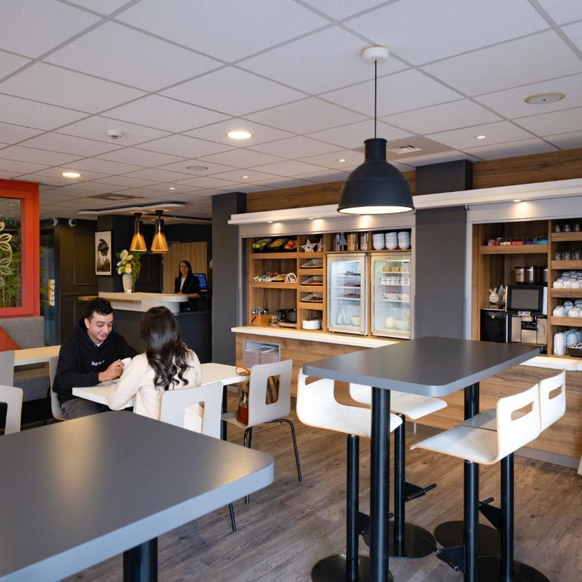 Un interior de cafetería moderna con mesas, sillas y una barra con exhibición de alimentos.