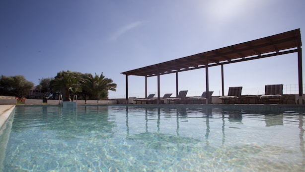 A clear swimming pool with lounge chairs under a pergola, surrounded by palm trees. - Aeraki Studios & Apartments (Naxos)