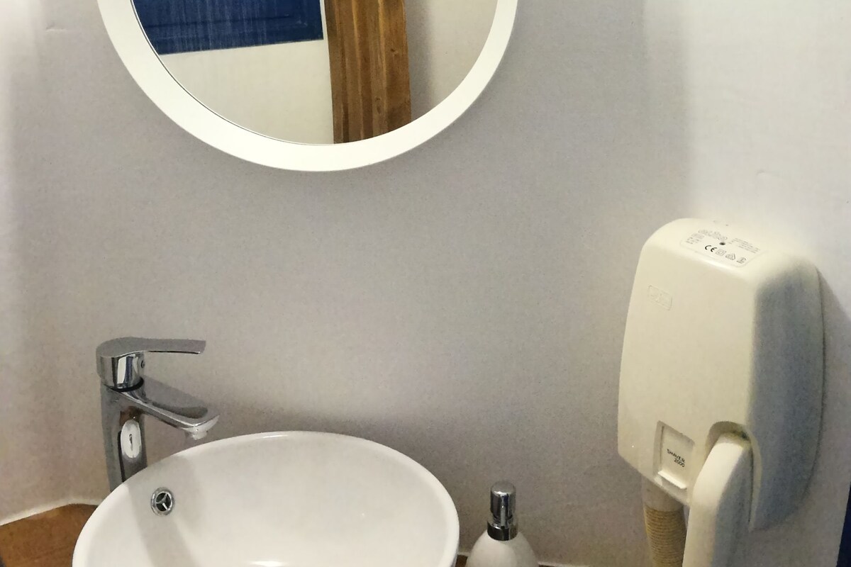 A bathroom with a round mirror, a white sink, a wooden countertop, a white soap dispenser, and a white telephone.