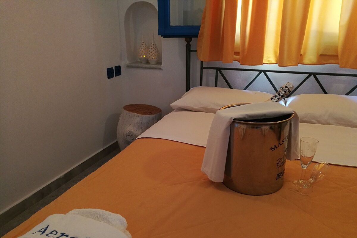 A hotel room with a bed, a metal bucket, a glass, and a towel with the name 'Aeraki' on it.