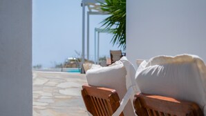 A wooden chair with a white cushion, a white pillow, and a wooden table in a sunny outdoor setting. - Aeraki Studios & Apartments (Naxos)