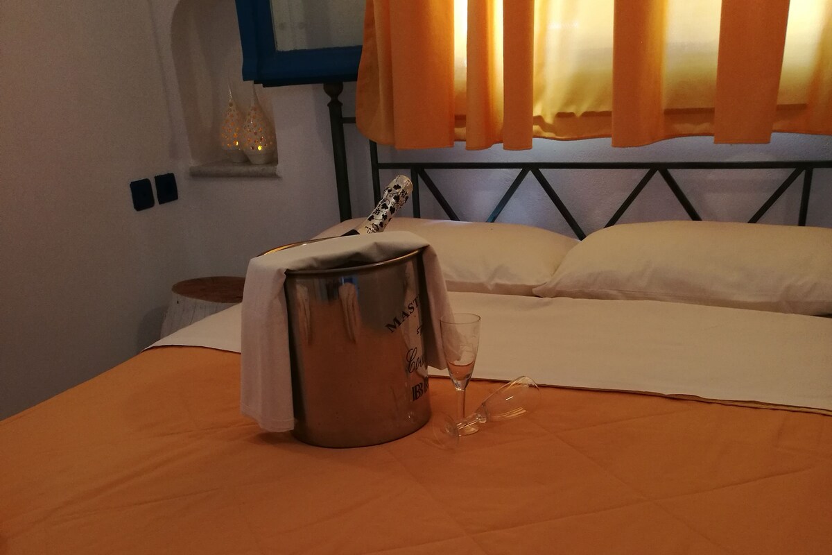 A neatly made bed with a folded towel labeled "Aeraki" and a metal container, possibly a minibar, on the bed.