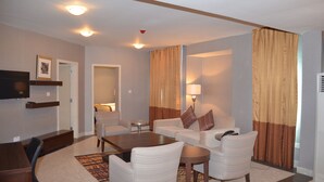 A hotel room with a dining table, two sofas, a TV, and a lamp. - Lakewood Luxury Apartment (Abuja)