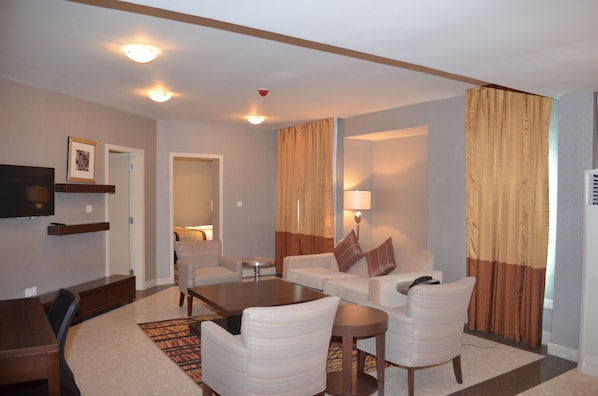 A hotel room with a dining table, two sofas, a TV, and a lamp.