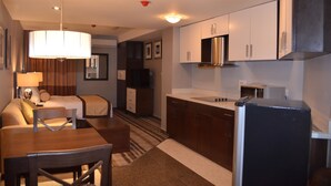 A compact hotel room with a kitchenette, a dining area, and a bed.