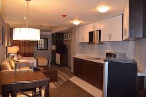 A compact hotel room with a kitchenette, a dining area, and a bed.