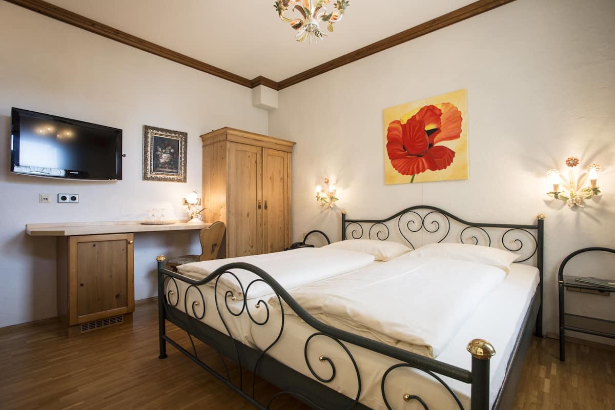 Un dormitorio con cama, televisor, aparador de madera y escritorio.
