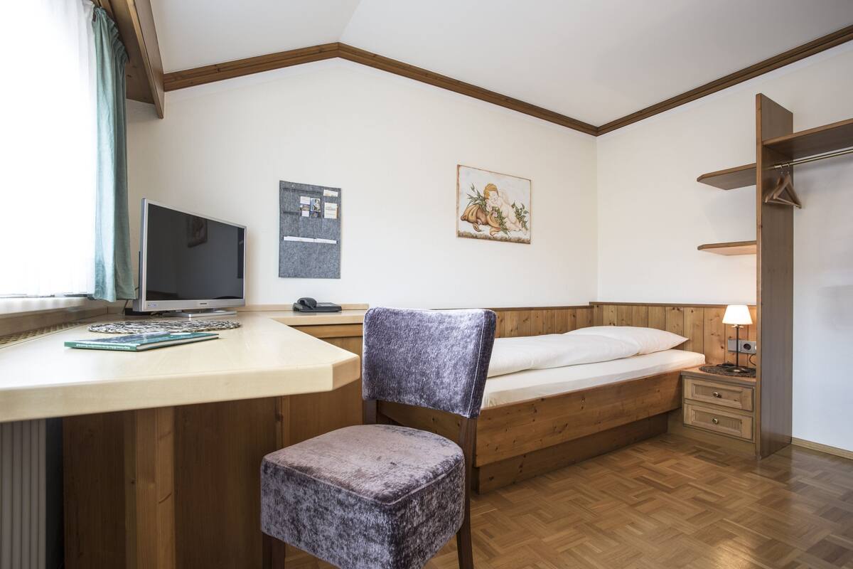 Un dormitorio con una cama de madera, un escritorio con una computadora, una silla y una mesita de noche con una lámpara.