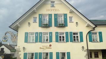 A hotel with a classic European architectural style, featuring a prominent 'HOTEL' sign at the top, multiple windows with shutters, and a balcony with a flower arrangement.
