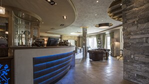 A spacious lobby with a curved reception desk, stone accents, and a seating area with a fireplace. - Meiser Rosenstuben Hotel (Fichtenau)