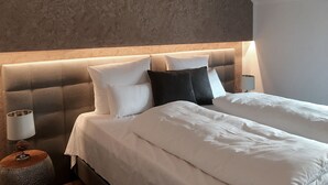 A neatly made bed with white and black pillows, a round bedside table with a lamp, and a textured wall in a hotel room. - Meiser Rosenstuben Hotel (Fichtenau)