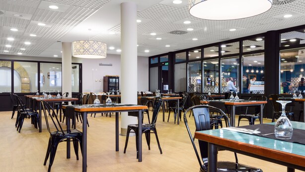 A spacious restaurant with multiple tables and chairs, large windows, and modern lighting fixtures. - Hospedium Hotel Don Fidel (Cuarte de Huerva)