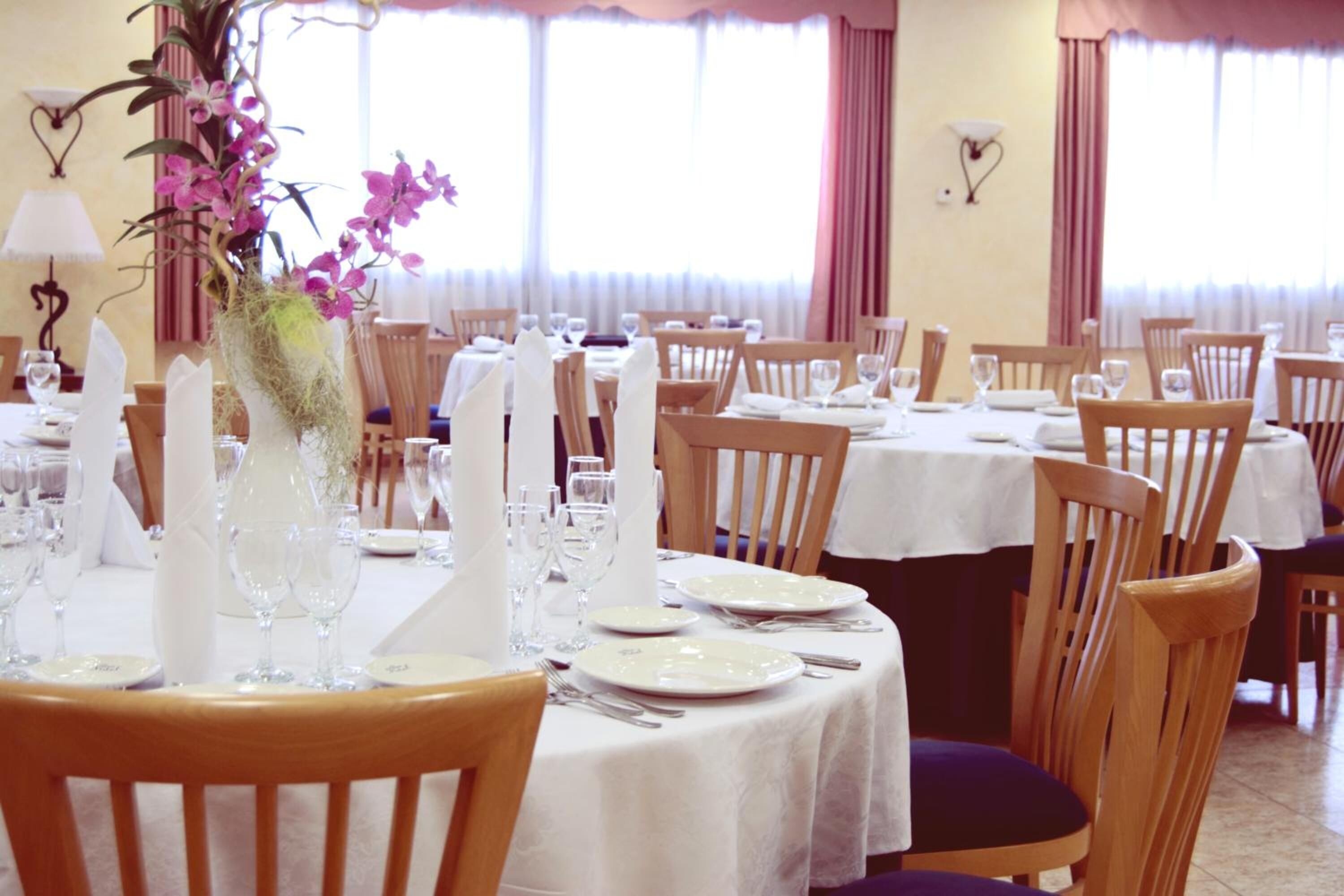 Un comedor con mesas dispuestas para el servicio, sillas y un jarrón con flores.