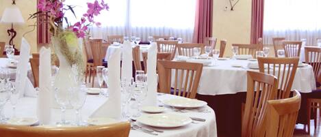 Un comedor con mesas dispuestas para el servicio, sillas y un jarrón con flores.