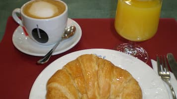 Un croissant en un plato, una taza de café con una cuchara y un vaso de jugo de naranja sobre una mesa.