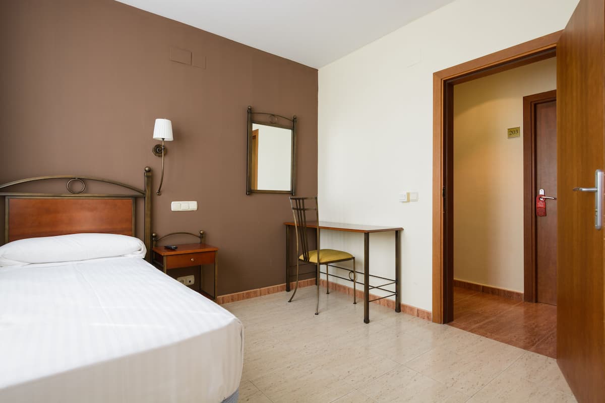 Una habitación de hotel con cama, escritorio, silla, espejo y puerta.