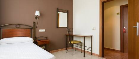 Una habitación de hotel con cama, escritorio, silla, espejo y puerta.