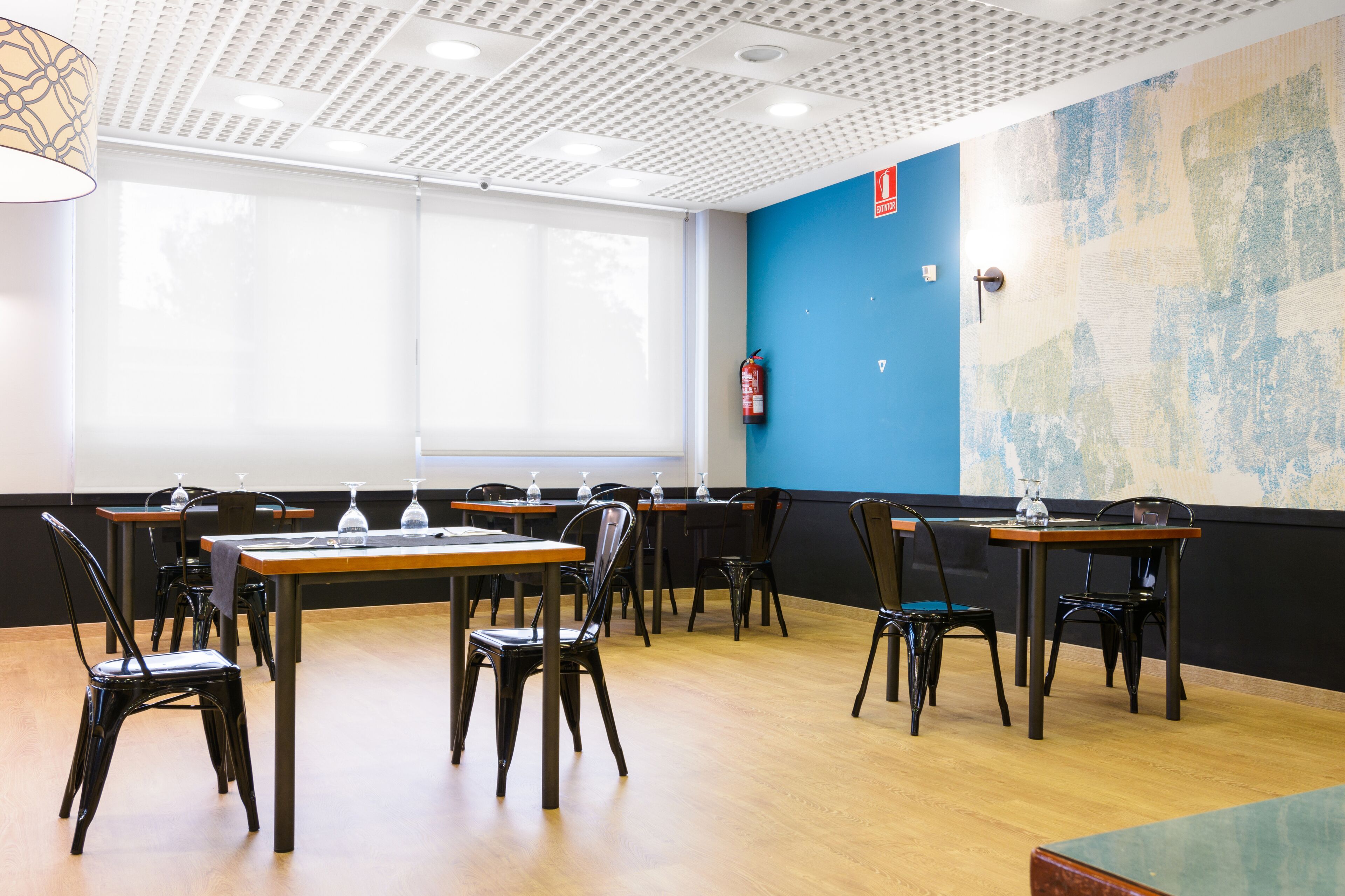 Un comedor con mesas y sillas, un extintor y una pared azul con textura.