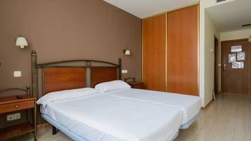 Cama doble con cabecera de madera, mesita de noche y un armario con espejo y una puerta que tiene un aviso.