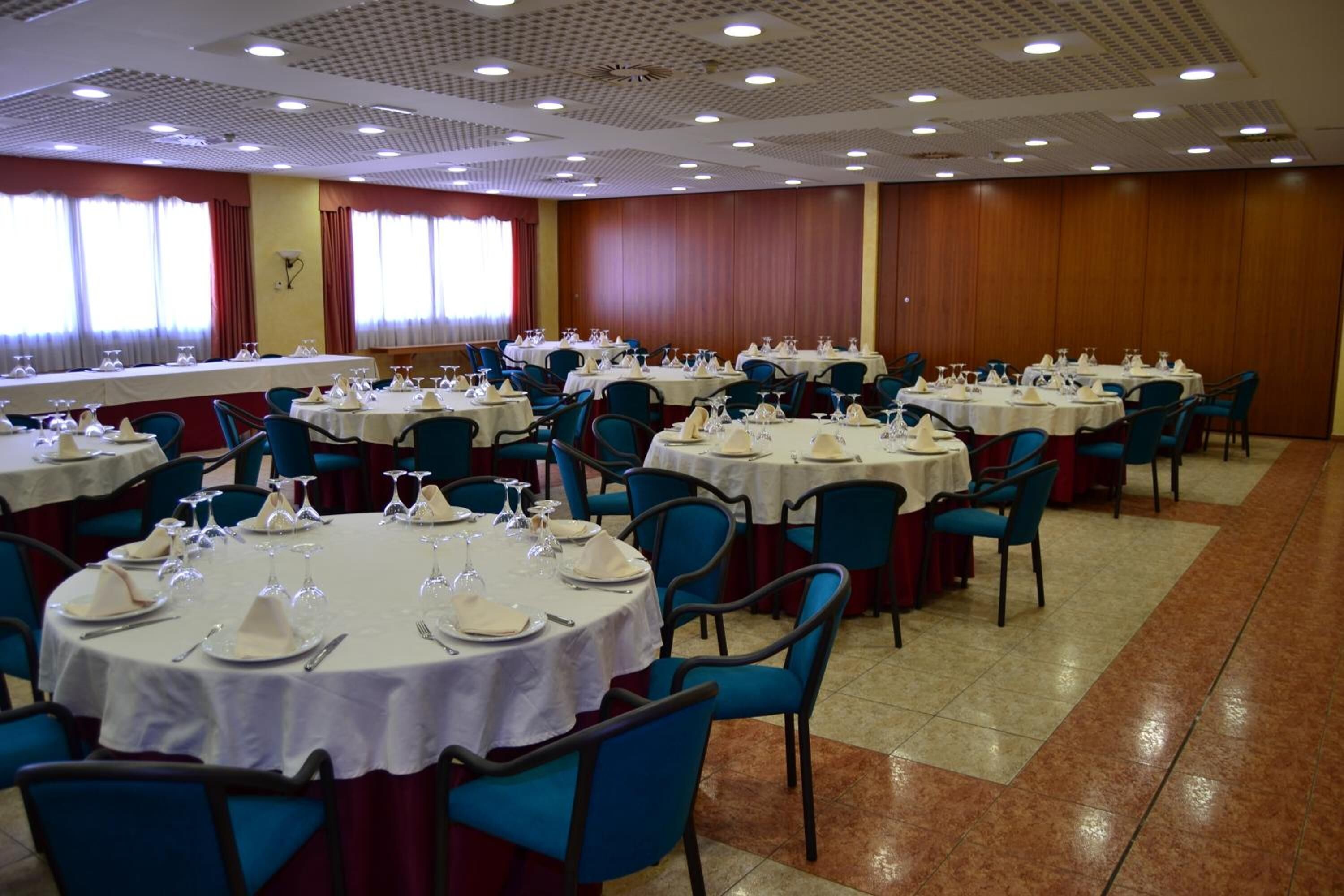 A banquet hall with round tables set for dining, blue chairs, and a long table with a white tablecloth.