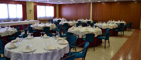 A banquet hall with round tables set for dining, blue chairs, and a long table with a white tablecloth.