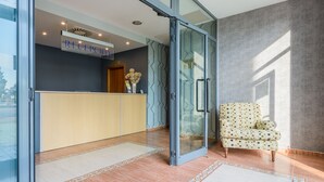 A reception area with a glass door, a reception desk, and a patterned armchair. - Hospedium Hotel Don Fidel (Cuarte de Huerva)