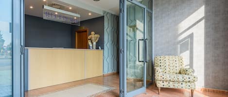 Un área de recepción con puerta de vidrio, mostrador de recepción y un sillón estampado.