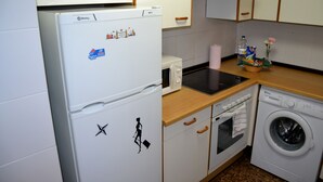 A compact kitchen with a refrigerator, microwave, oven, and washing machine. - Apartamentos Dos Torres Barbol (Zaragoza)