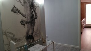 A room with a large tree mural on the wall, a small table with a lamp, and a window with a view of the outside. - Apartamentos Dos Torres Barbol (Zaragoza)