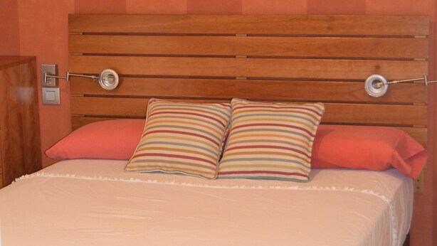 A bedroom with a wooden headboard, two pillows, and three wall-mounted paintings of cherubs. - Apartamentos Dos Torres Barbol (Zaragoza)