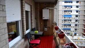 A balcony with a red floor, a table with chairs, and potted plants. - Apartamentos Dos Torres Barbol (Zaragoza)