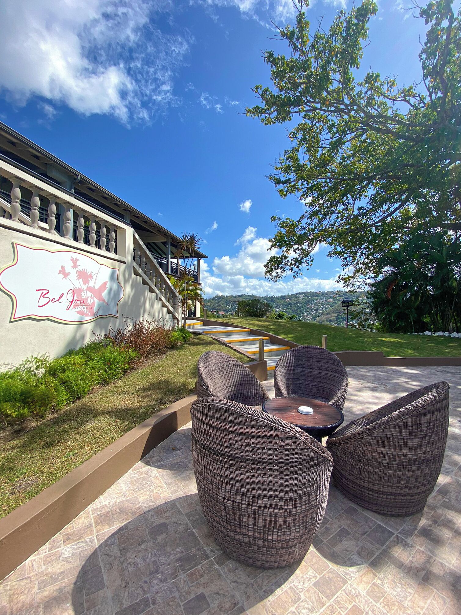 An outdoor seating area with wicker furniture, a stone-tiled patio, and a view of a building with a sign.