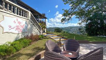 An outdoor seating area with wicker furniture, a stone-tiled patio, and a view of a building with a sign.