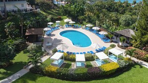 A circular pool with lounge chairs and umbrellas, surrounded by lush greenery and palm trees. - Bel Jou Hotel – Adults Only – All Inclusive (Castries)