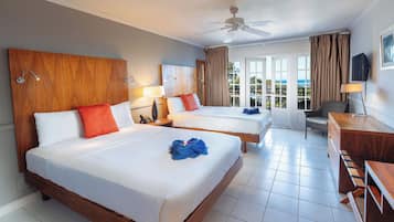 Habitación de hotel con dos camas, ventilador de techo, escritorio y vistas al exterior.