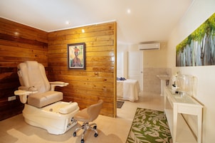 Quarto com cadeira de massagem, pintura, pia e mesa de vidro.