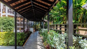 A covered walkway with a wooden ceiling, surrounded by lush greenery and potted plants. - Bel Jou Hotel – Adults Only – All Inclusive (Castries)