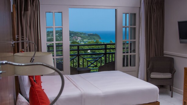 A hotel room with a bed, a chair, a TV, and a balcony with a view of the ocean. - Bel Jou Hotel – Adults Only – All Inclusive (Castries)