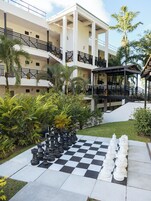 Un patio con un tablero de ajedrez y piezas, rodeado de palmeras y un edificio de varios pisos con balcones.